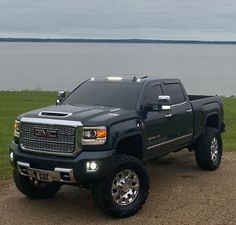 a black truck parked on top of a dirt road next to a body of water