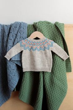 two knitted sweaters are hanging on a clothes rack, one is green and the other is blue