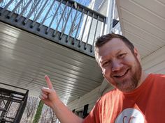 a man in an orange shirt is giving the peace sign while standing outside his house