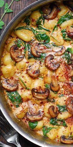 a pan filled with potatoes and mushrooms on top of a wooden table next to silverware