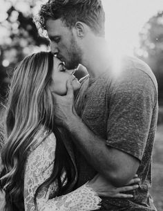 a man and woman kissing each other in the grass with trees in the back ground