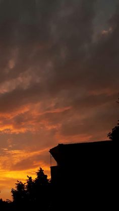 an airplane flying in the sky at sunset with clouds and trees behind it as the sun is setting