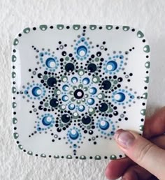 a hand holding a small decorative plate with blue and green designs on it's surface