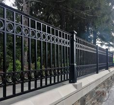 a black iron fence on the side of a stone wall with trees in the background