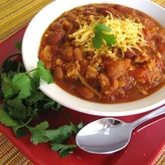 a white bowl filled with chili and beans on top of a red plate next to cilantro