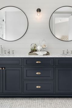 two round mirrors are above the double sink vanity in this white and blue bathroom with black cabinets