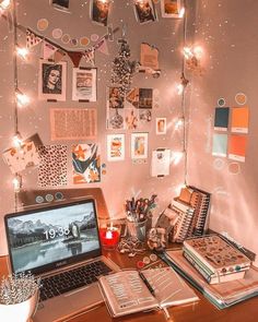 an open laptop computer sitting on top of a wooden desk next to a wall covered in pictures