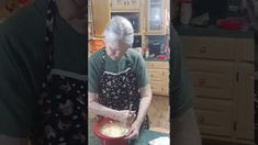 an older woman is preparing food in the kitchen while wearing an apron and holding a red bowl