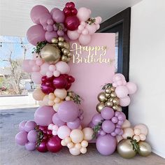 a pink and gold balloon arch with happy birthday written on the front door, surrounded by balloons