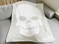 a white crocheted blanket with a skull on it sitting on a gray couch