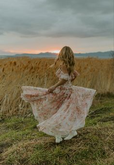 a woman in a floral dress walking through a field at sunset with her hair blowing in the wind