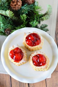 three small pastries on a white plate with pine cones and evergreen branches in the background