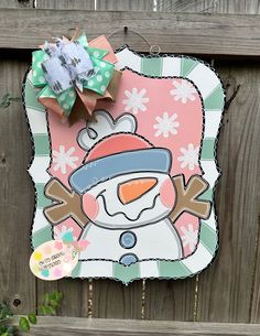 a paper snowman hanging on the side of a wooden fence with a tag attached to it