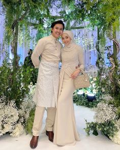 two people standing next to each other in front of flowers and greenery at an event