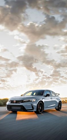 a silver car driving down a road under a cloudy sky