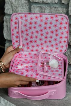 a woman is holding a pink suitcase with items in it and her hand on the lid