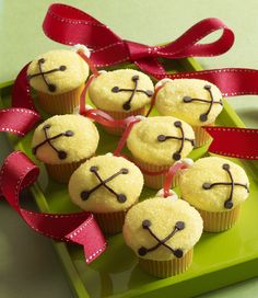 some cupcakes with faces on them are sitting on a green plate and red ribbon