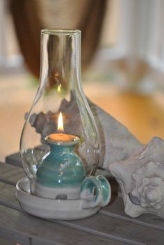 a glass vase with a lit candle in it sitting on a table next to seashells