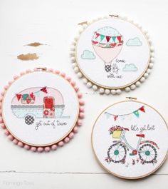 three cross stitch hoops with embroidered pictures on them, one has a bicycle and the other has a hot air balloon