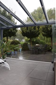 an outdoor patio with tables and chairs in the rain, surrounded by greenery on either side