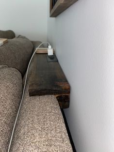 a couch with a cord connected to it and a wooden shelf on the wall behind it