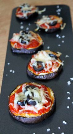 mini pizzas with cheese and olives on a black tray