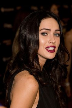 a woman with long dark hair wearing a black dress and red lipstick on her lips