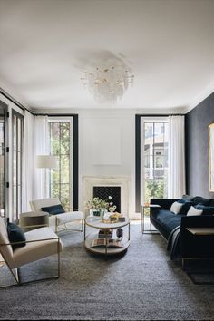 a living room filled with furniture and a chandelier above a fire place in front of two windows