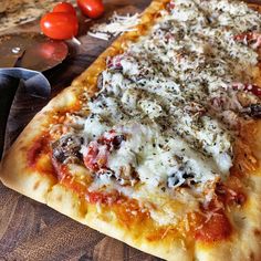 a pizza sitting on top of a wooden cutting board next to a knife and tomatoes