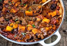 a pot full of stew with a spoon in it and two plates on the side