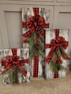 three wooden blocks decorated with red and black plaid bows, pine cones and evergreen branches