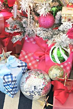 presents wrapped in red and white paper under a christmas tree with ornaments around it,