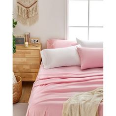 a bed with pink sheets and pillows next to a window