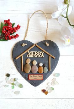 a slate heart shaped ornament with the words merry christmas on it and rocks in front