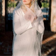 a woman in a white wedding dress and veil with her hands on her chest looking off to the side