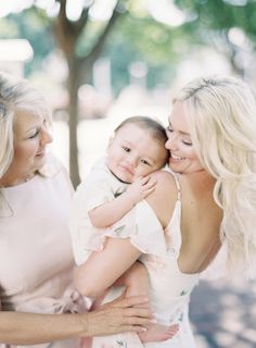 two women and a baby are smiling at each other while the woman is holding her