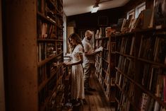 a man and woman standing in front of a bookshelf filled with lots of books