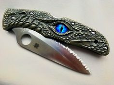 a knife with an eye on it sitting next to a knife blade that looks like a dragon's head