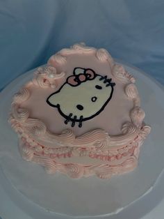 a hello kitty cake with pink icing on a white plate and blue table cloth