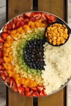 a platter filled with fruit and cereals on top of a wooden table next to a spoon