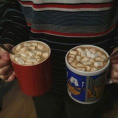 two cups of hot chocolate with marshmallows in them are being held by someone