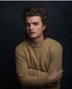 a young man with his arms crossed posing for a photo in front of a black background