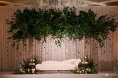 a white couch sitting in front of a lush green tree filled with flowers and candles