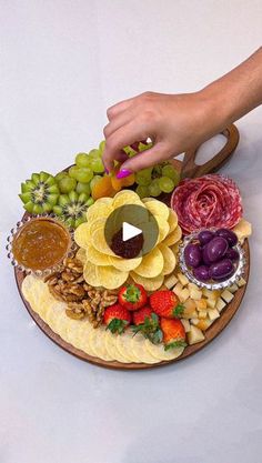 a platter with fruit, nuts and crackers is being held by a woman's hand