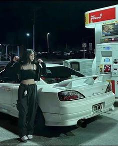 a woman standing next to a white car at a gas station