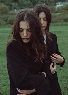 two women standing next to each other in a field, one holding her arms around the other