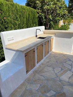 an outdoor kitchen is built into the side of a building with stone flooring and white walls