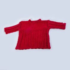 a red sweater is laying on the white surface, it looks like an old fashioned sweater