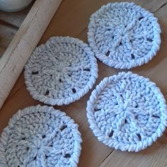 four crocheted coasters sitting on top of a wooden table