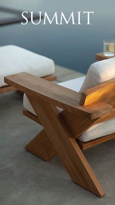 a wooden lounge chair sitting on top of a cement floor next to a table with white pillows